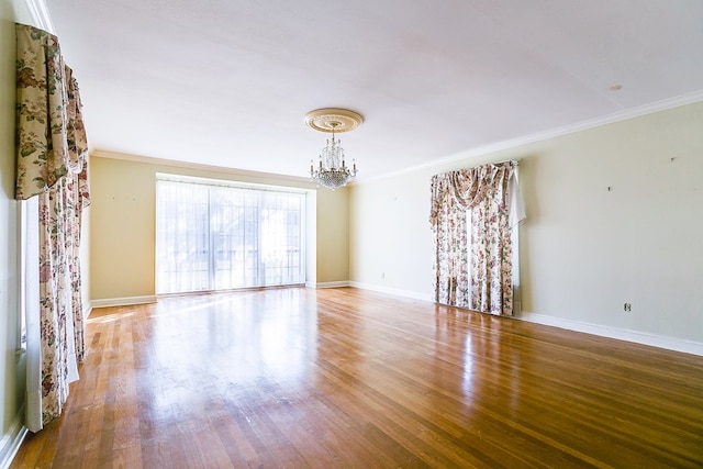 empty room featuring a chandelier, baseboards, wood finished floors, and crown molding