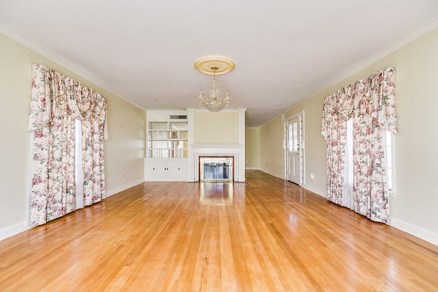 unfurnished living room featuring ornamental molding, a fireplace, light wood-style flooring, and a notable chandelier