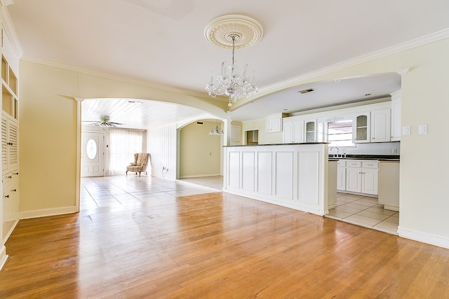 unfurnished living room featuring arched walkways, a sink, baseboards, light wood-style floors, and ornamental molding