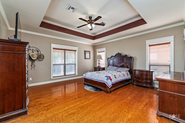 bedroom with crown molding, wood-type flooring, and a raised ceiling