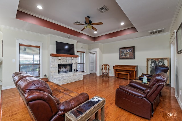 living room with crown molding, a tray ceiling, ceiling fan, a fireplace, and hardwood / wood-style floors