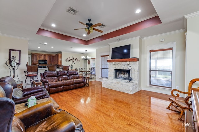 living room with a fireplace, ceiling fan with notable chandelier, light hardwood / wood-style flooring, and a raised ceiling