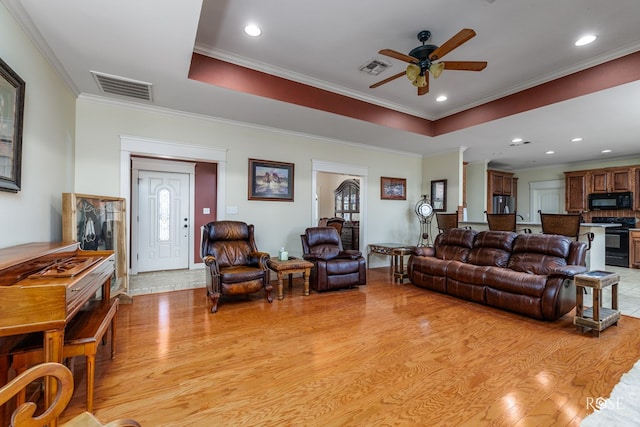 living room with crown molding, light hardwood / wood-style floors, a raised ceiling, and ceiling fan