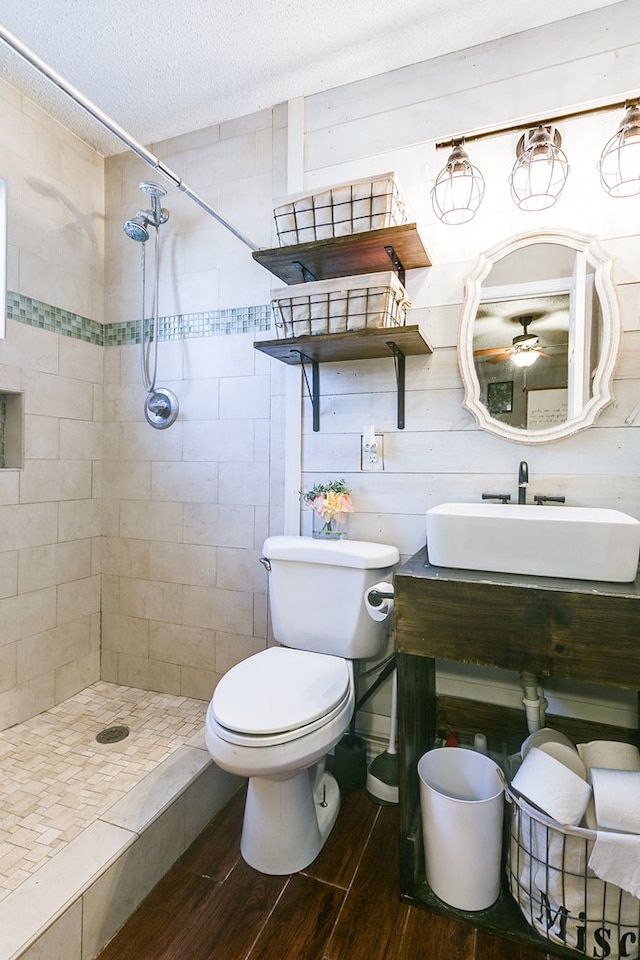 bathroom with wooden walls, tiled shower, vanity, a textured ceiling, and toilet