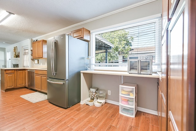 kitchen with ornamental molding, appliances with stainless steel finishes, a textured ceiling, and light hardwood / wood-style floors