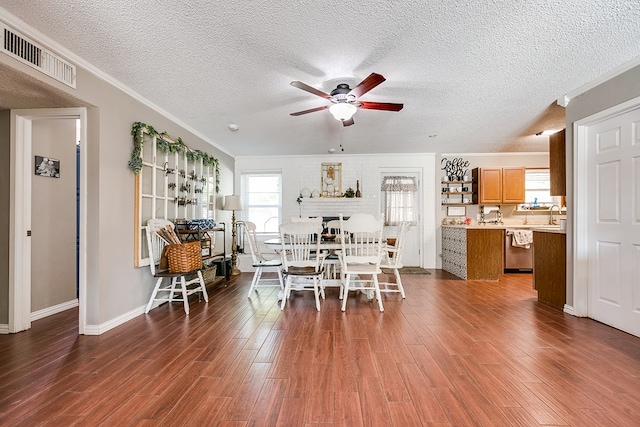 dining area featuring dark hardwood / wood-style flooring, ceiling fan, crown molding, a brick fireplace, and a textured ceiling