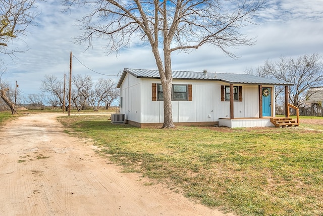 view of front of home with dirt driveway, metal roof, a front lawn, and cooling unit