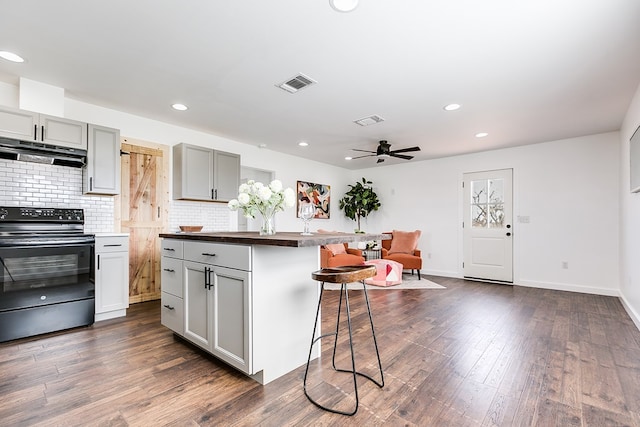 kitchen with a breakfast bar, visible vents, black range with electric stovetop, gray cabinetry, and under cabinet range hood