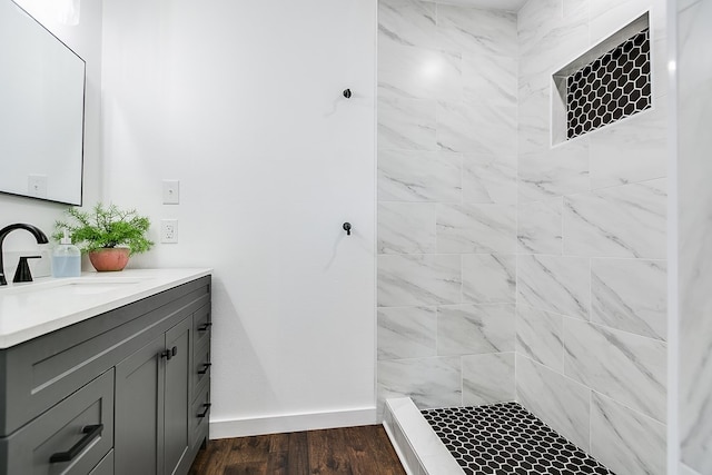 bathroom featuring baseboards, a tile shower, wood finished floors, and vanity