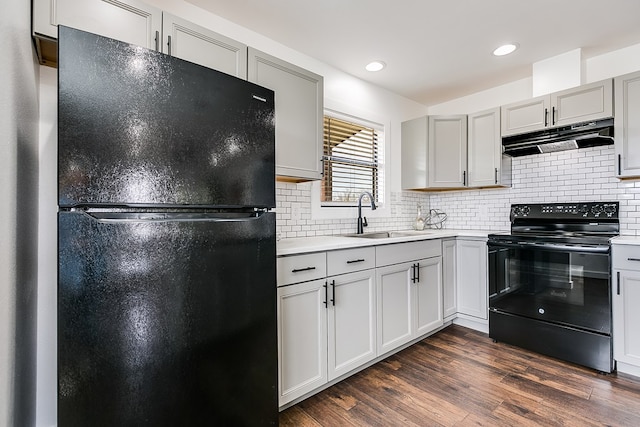 kitchen featuring under cabinet range hood, dark wood-style flooring, a sink, decorative backsplash, and black appliances