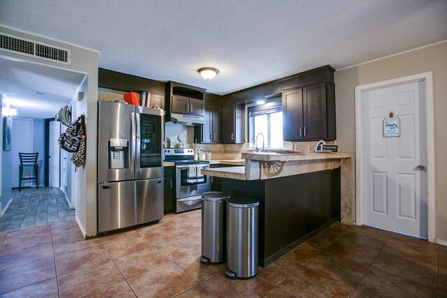 119 Van Zandt St, San Angelo, TX 76905 - kitchen featuring appliances with stainless steel finishes, a textured ceiling, light countertops, a peninsula, and under cabinet range hood