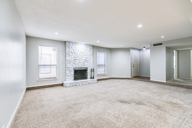 unfurnished living room featuring carpet, visible vents, a stone fireplace, a textured ceiling, and baseboards