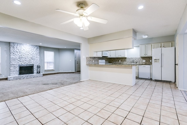 kitchen featuring ceiling fan, a stone fireplace, light colored carpet, white appliances, and decorative backsplash