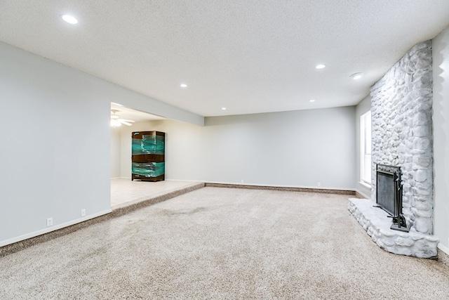 unfurnished living room with carpet floors, baseboards, a textured ceiling, and a stone fireplace