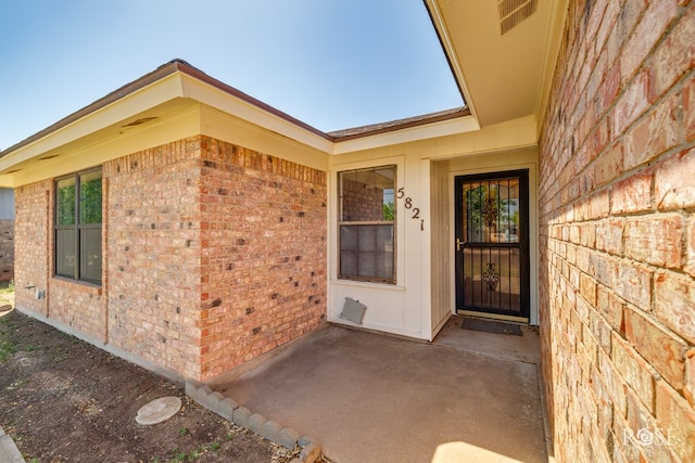 doorway to property with brick siding, a patio area, and visible vents