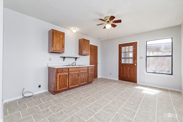 kitchen featuring a ceiling fan, a textured ceiling, brown cabinets, light countertops, and a sink