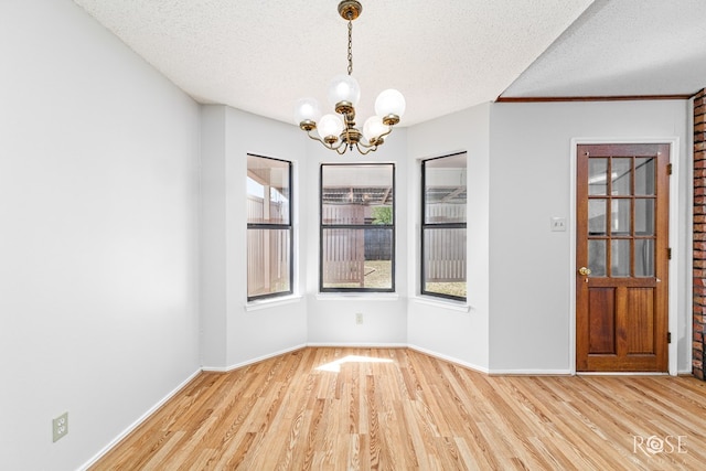 unfurnished dining area featuring a textured ceiling, a notable chandelier, baseboards, and light wood finished floors