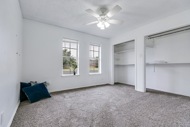 unfurnished bedroom featuring carpet flooring, two closets, a textured ceiling, and ceiling fan