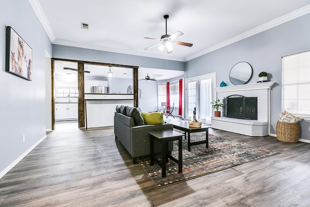 living room featuring wood-type flooring, a brick fireplace, ceiling fan, and crown molding