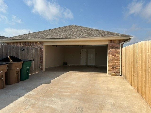exterior space with brick siding, fence, roof with shingles, and a garage