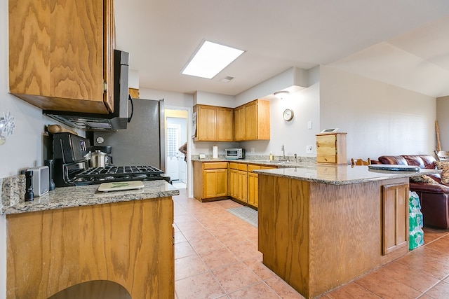 kitchen with light stone counters, sink, kitchen peninsula, and stove