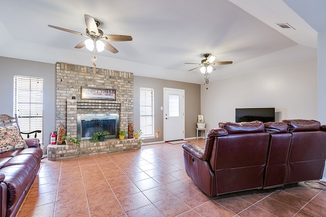 tiled living room featuring a raised ceiling, a brick fireplace, and ceiling fan