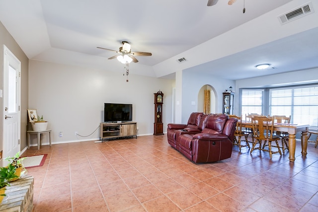 living room featuring a raised ceiling, light tile patterned floors, and ceiling fan