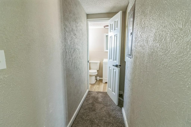 corridor with light colored carpet and a textured ceiling