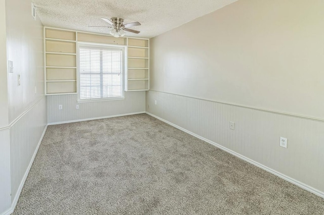 empty room featuring ceiling fan, light colored carpet, built in features, and a textured ceiling