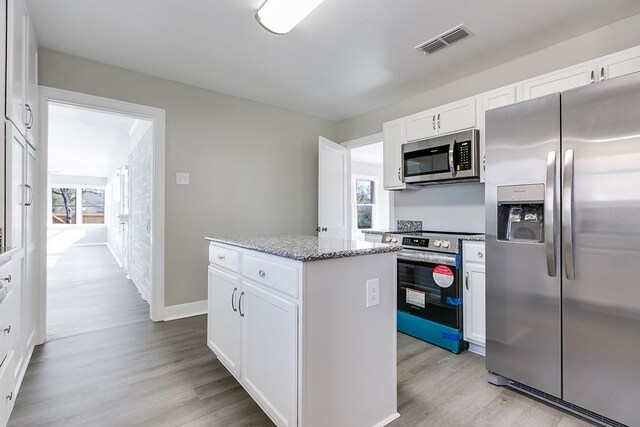 kitchen with appliances with stainless steel finishes, white cabinetry, a center island, light stone counters, and light hardwood / wood-style floors