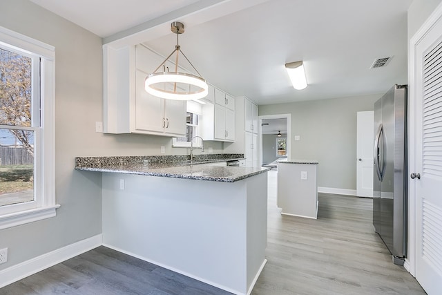 kitchen with white cabinetry, decorative light fixtures, stainless steel fridge, and kitchen peninsula