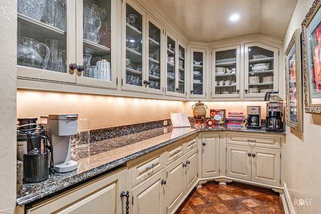 bar with dark stone countertops, cream cabinets, and vaulted ceiling