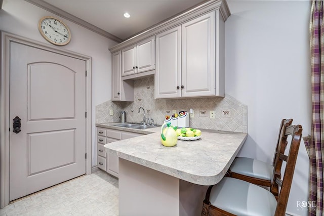 kitchen featuring sink, crown molding, backsplash, a kitchen breakfast bar, and kitchen peninsula