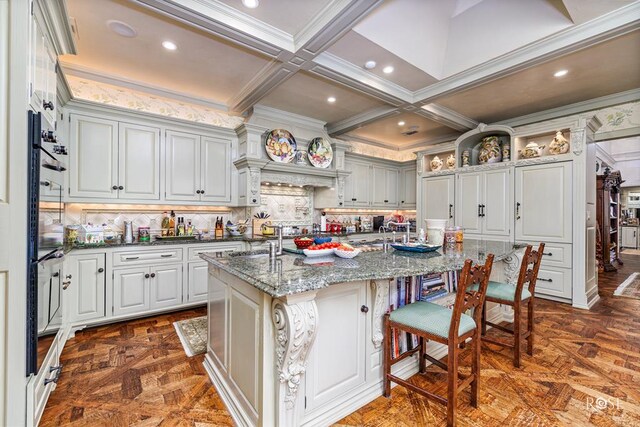 kitchen featuring dark parquet floors, beamed ceiling, an island with sink, dark stone countertops, and a kitchen bar