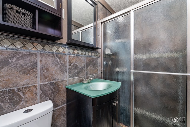 bathroom with a shower with shower door, tile walls, vanity, toilet, and a textured ceiling