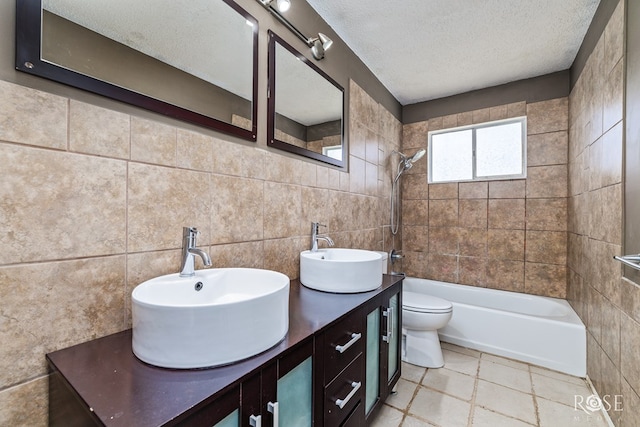 full bathroom featuring tile walls, vanity, a textured ceiling, tiled shower / bath, and toilet