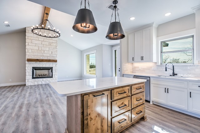 kitchen featuring decorative light fixtures, dishwasher, white cabinets, a center island, and light stone countertops