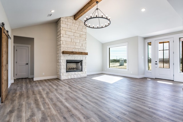 unfurnished living room featuring a stone fireplace, a chandelier, lofted ceiling with beams, a barn door, and hardwood / wood-style floors