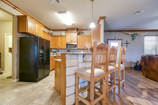 kitchen featuring a kitchen bar, hanging light fixtures, ornamental molding, light stone counters, and black refrigerator with ice dispenser