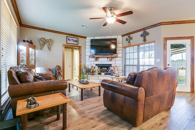 living room featuring ornamental molding, a stone fireplace, ceiling fan, and light hardwood / wood-style floors