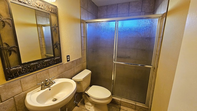 bathroom featuring a shower with shower door, sink, tile walls, toilet, and tile patterned floors