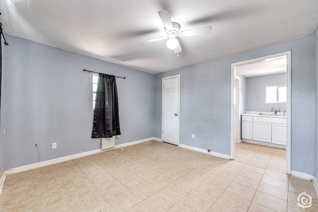 unfurnished bedroom featuring ceiling fan, baseboards, a sink, and ensuite bathroom