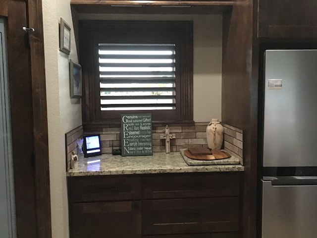 kitchen featuring tasteful backsplash, stainless steel fridge, dark brown cabinetry, and light stone counters