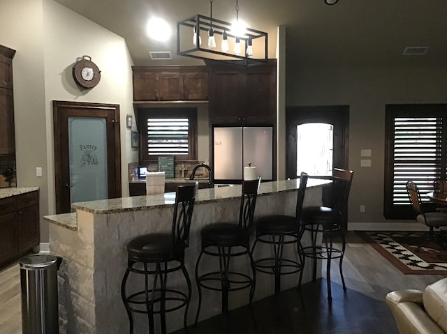 kitchen featuring stainless steel fridge, an island with sink, pendant lighting, light stone countertops, and light hardwood / wood-style floors