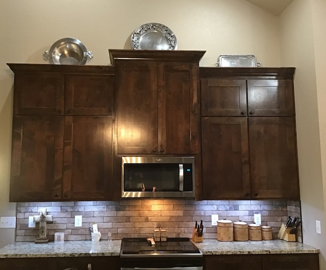 kitchen with tasteful backsplash, light stone counters, vaulted ceiling, and cooktop