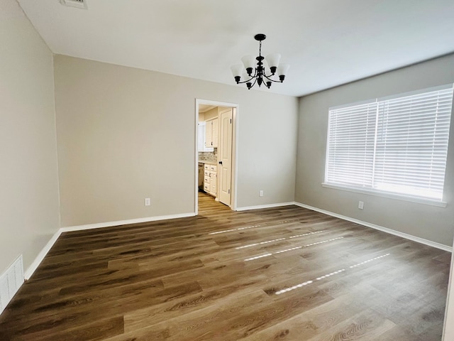 spare room with a chandelier and dark wood-type flooring