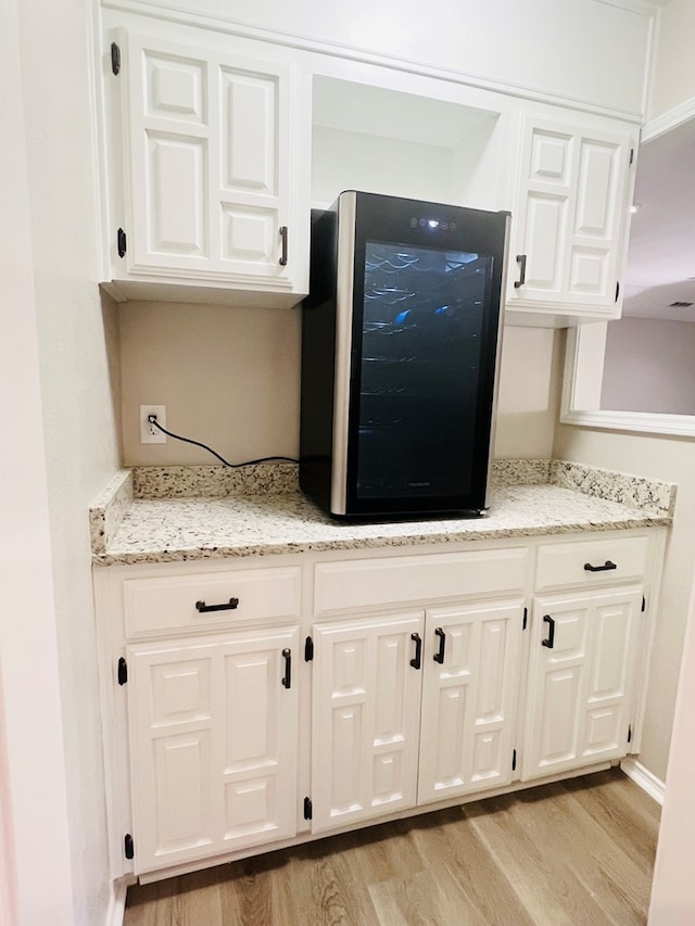 kitchen featuring light stone counters, beverage cooler, light hardwood / wood-style floors, and white cabinets