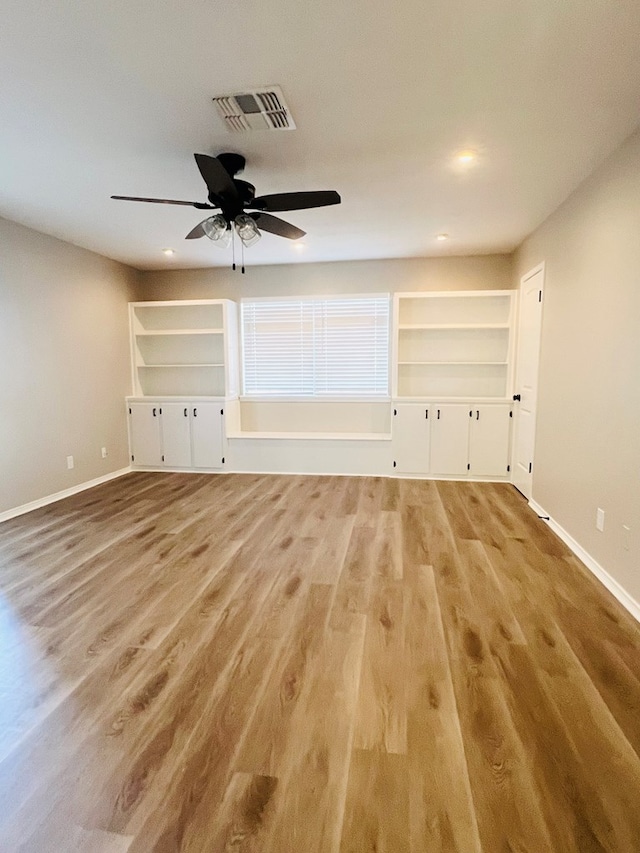 unfurnished room with built in shelves, ceiling fan, and light wood-type flooring