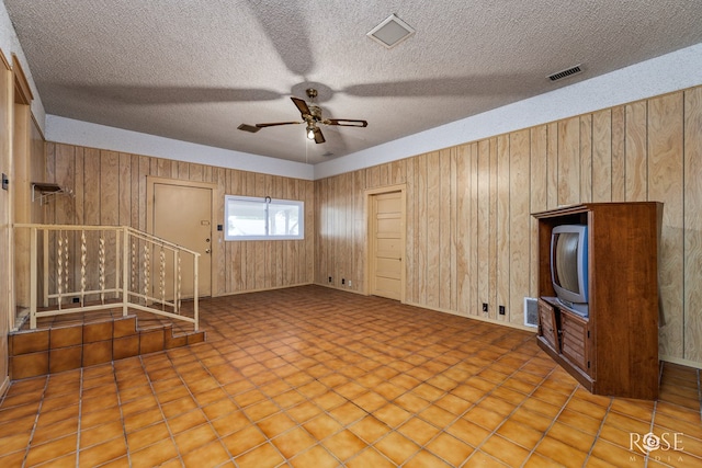 unfurnished living room featuring ceiling fan, a textured ceiling, and wood walls