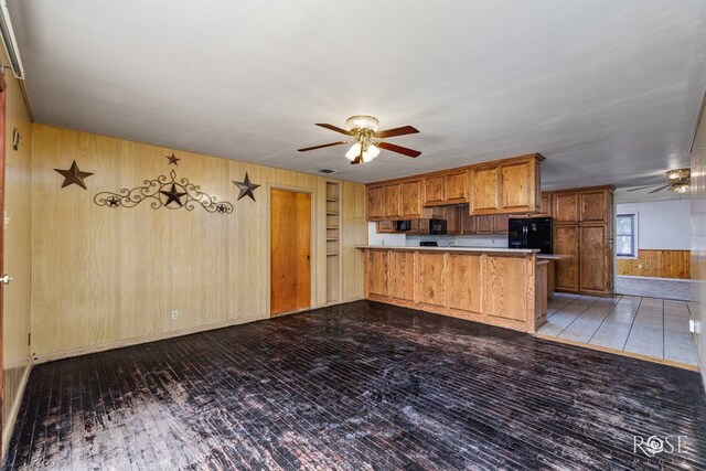 kitchen with built in features, ceiling fan, wooden walls, black fridge, and kitchen peninsula